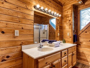 A wooden cabin bathroom with a white sink, mirror, and built-in cabinet. - Peaceful 2BR w/Hot Tub*Pool Table*Fireplace*Arcade (Sevierville)