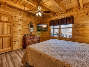 A wooden cabin bedroom with a bed, dresser, mirror, and a window with a view. - Peaceful 2BR w/Hot Tub*Pool Table*Fireplace*Arcade (Sevierville)