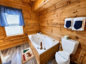 A wooden cabin bathroom with a bathtub, toilet, and a window with curtains. - Peaceful 2BR w/Hot Tub*Pool Table*Fireplace*Arcade (Sevierville)