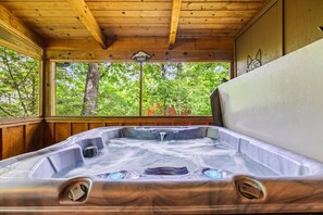 Un bain à remous dans un chalet en bois, avec vue sur les arbres à l’extérieur.