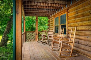 A wooden cabin with a porch, rocking chairs, and a view of the surrounding forest. - Peaceful 2BR w/Hot Tub*Pool Table*Fireplace*Arcade (Sevierville)
