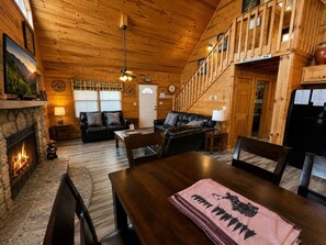 A log cabin interior with a fireplace, wooden walls, a dining area, and a loft bedroom. - Peaceful 2BR w/Hot Tub*Pool Table*Fireplace*Arcade (Sevierville)