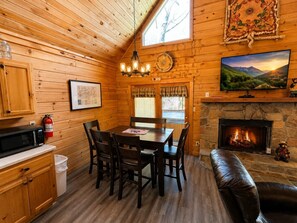 A wooden cabin interior with a dining table, chairs, a fireplace, a television, and a stone fireplace surround. - Peaceful 2BR w/Hot Tub*Pool Table*Fireplace*Arcade (Sevierville)