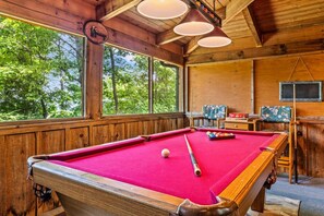 Une table de billard avec des billes, un tableau noir et une fenêtre donnant sur des arbres.