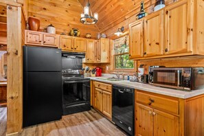 Une cuisine compacte avec des meubles en bois, un réfrigérateur noir, une cuisinière, un lave-vaisselle et un four à micro-ondes.