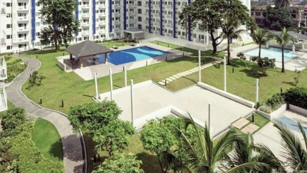 Een hoog appartementencomplex met meerdere balkons, een zwembad en veel groen eromheen.