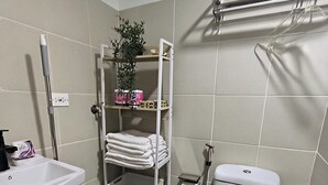 Een badkamer met een wit wastafelmeubel, toilet, handdoekhouder, plank met toiletartikelen en een plant.