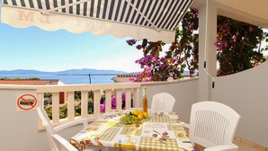 Un balcone con un tavolo apparecchiato per due persone, una bottiglia e una ciotola di frutta.