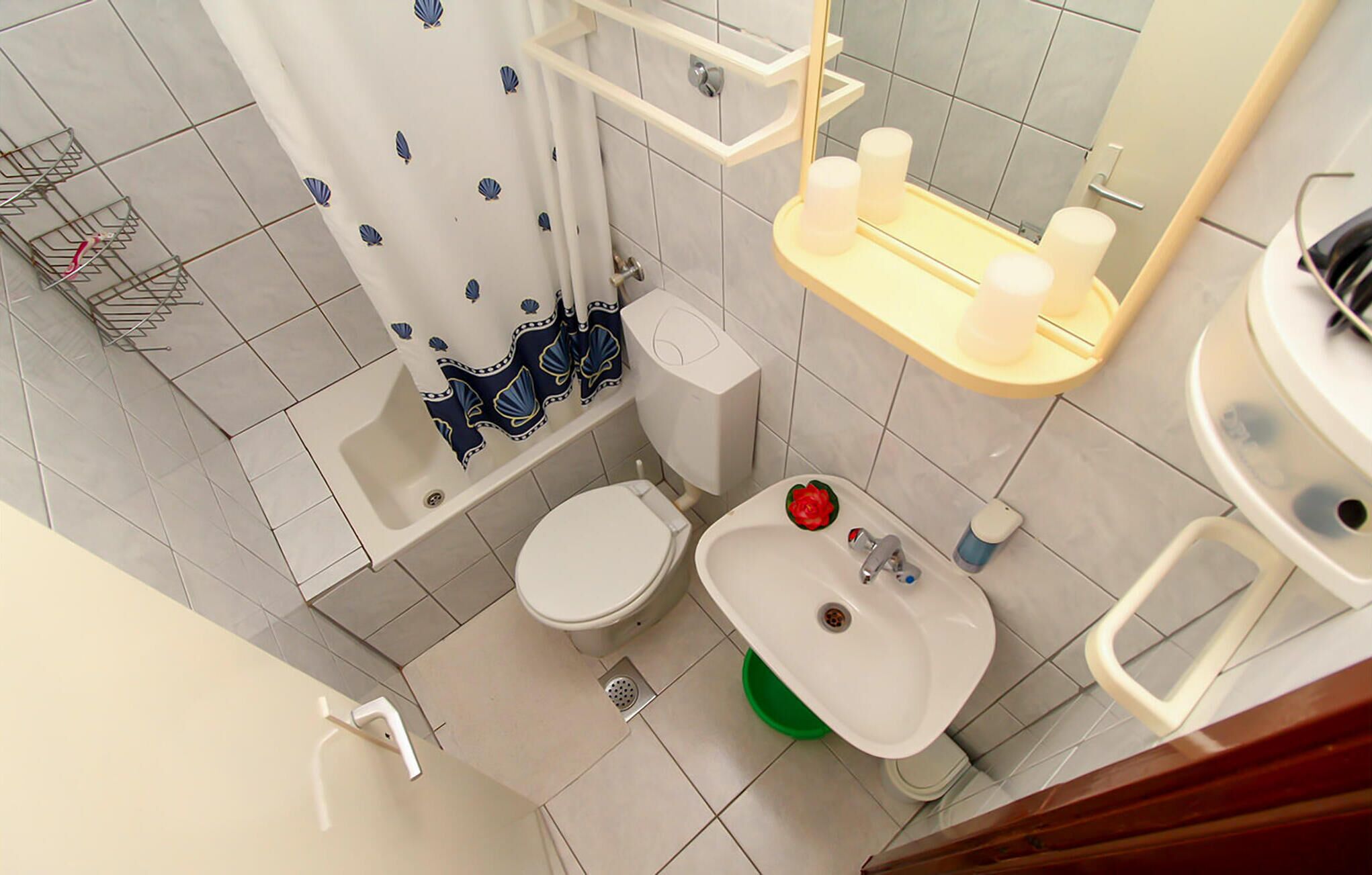 Een badkamer met toilet, wastafel en douche. Er is een handdoekhouder en een spiegel boven de wastafel.
