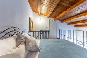 Un dormitori amb un llit, un sostre de fusta, una barana metàl·lica i una porta.