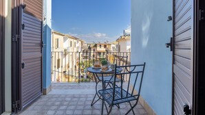 Uma varanda com mesa e cadeiras, vista para edifícios e um portão fechado.