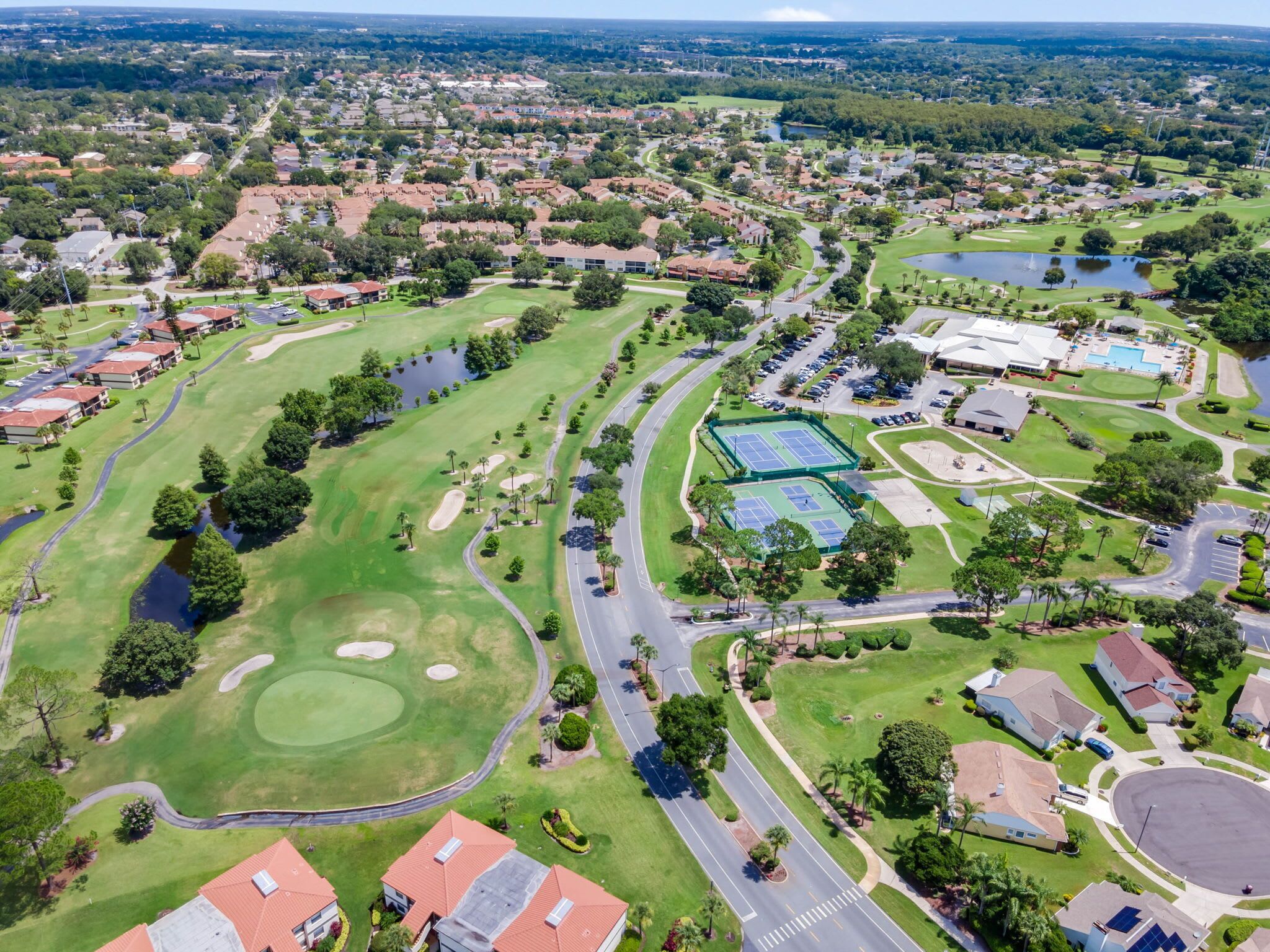 Vista aérea de um campo de golfe com um lago grande, quadras de tênis e áreas residenciais.
