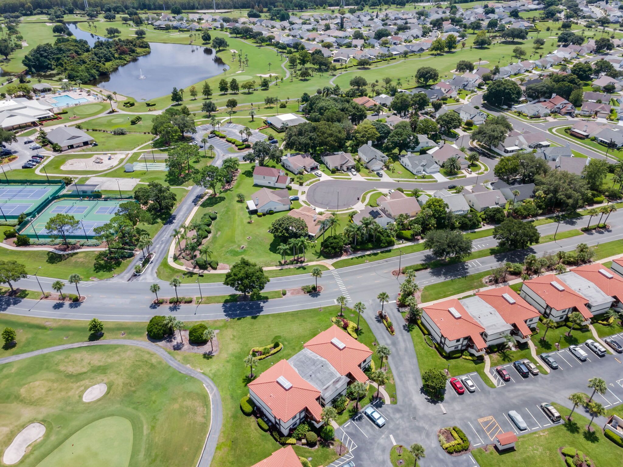 An aerial view of a residential area with houses, roads, a golf course, and a swimming pool.