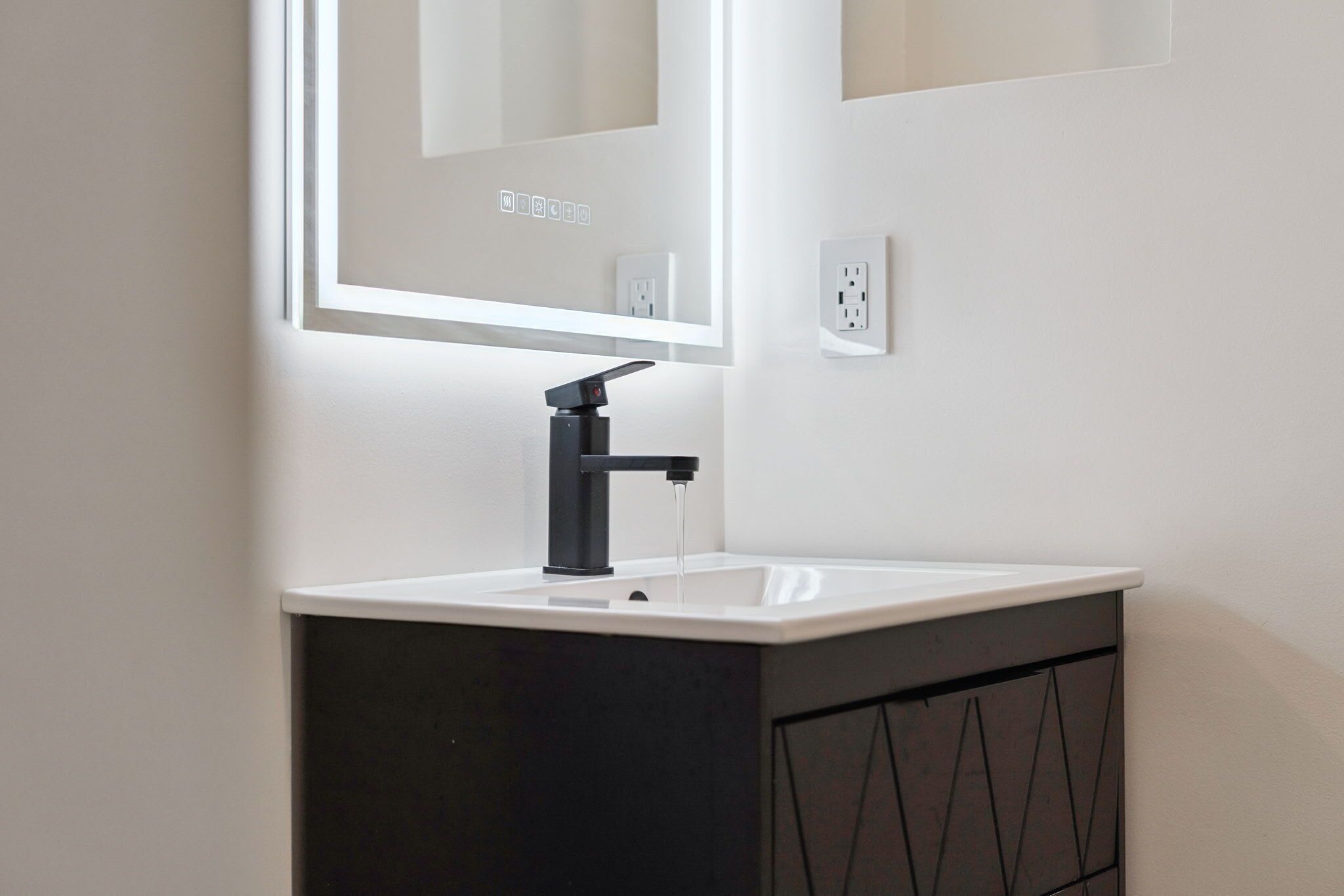 Een moderne badkamer met een wit wastafel, een zwarte kraan en een spiegel erboven.