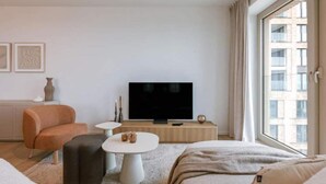 A modern hotel room with a large window, a flat-screen TV, a sofa, a coffee table, and a small side table. - Nora - Elegant Seaview Escape With Balcony (Ostend)