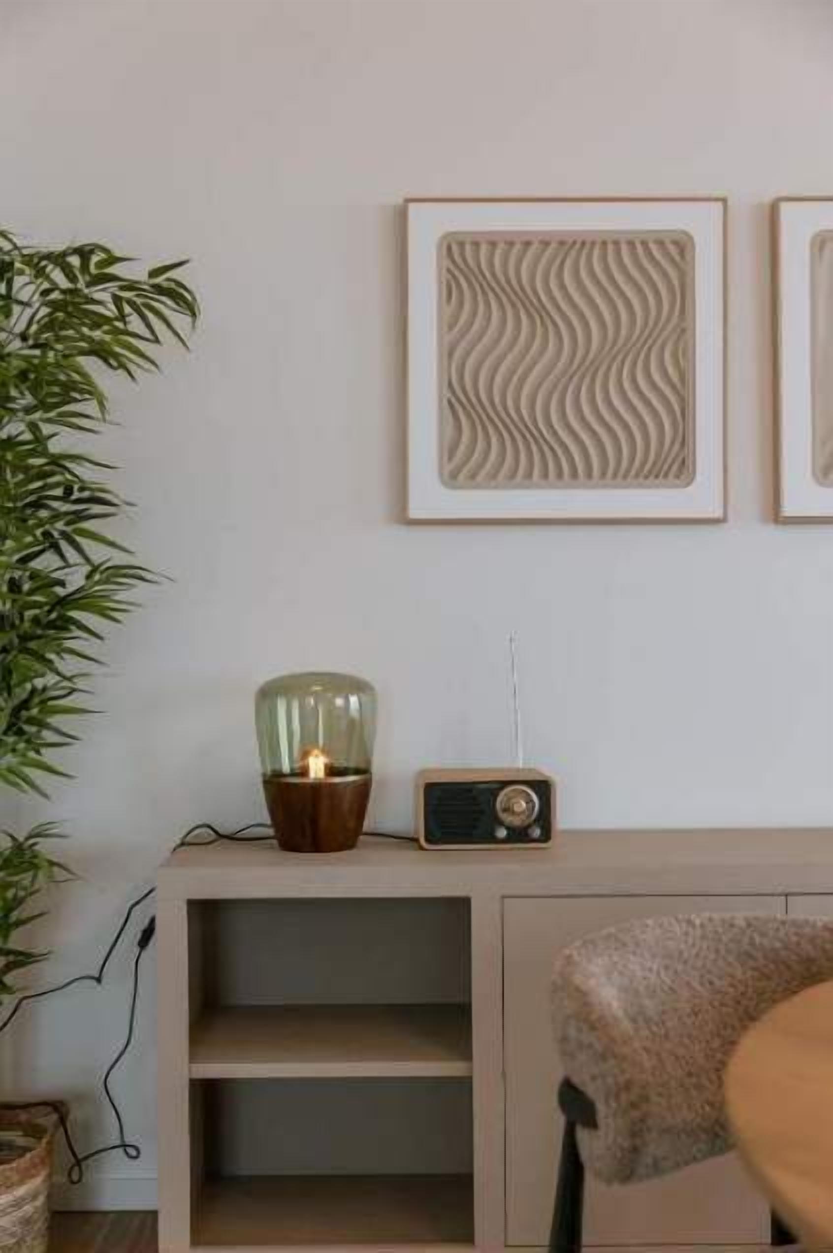 Une pièce comprenant un meuble en bois, une radio, une lampe et une œuvre d’art encadrée accrochée au mur.