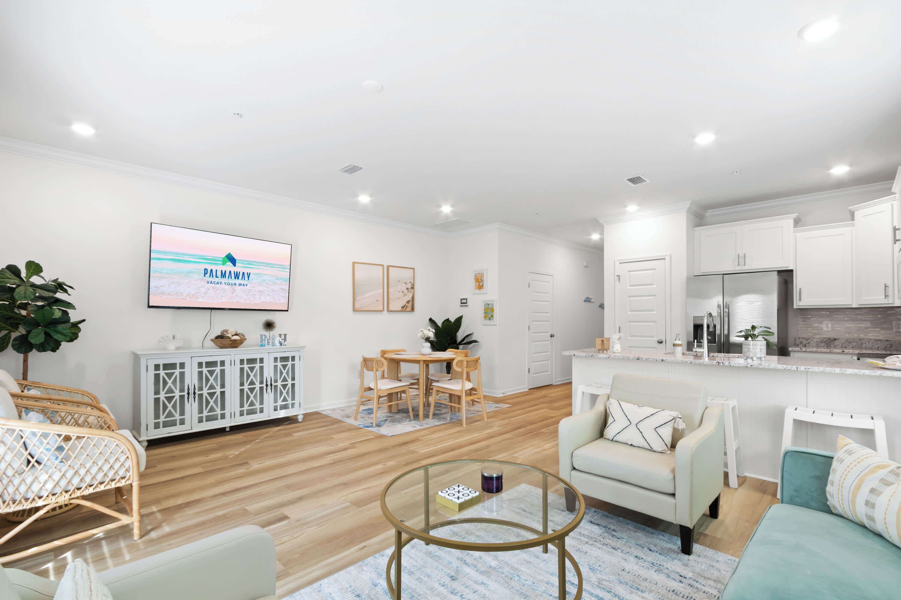 A modern living room with a dining area, kitchen, and a TV displaying 'PALMWAY'.