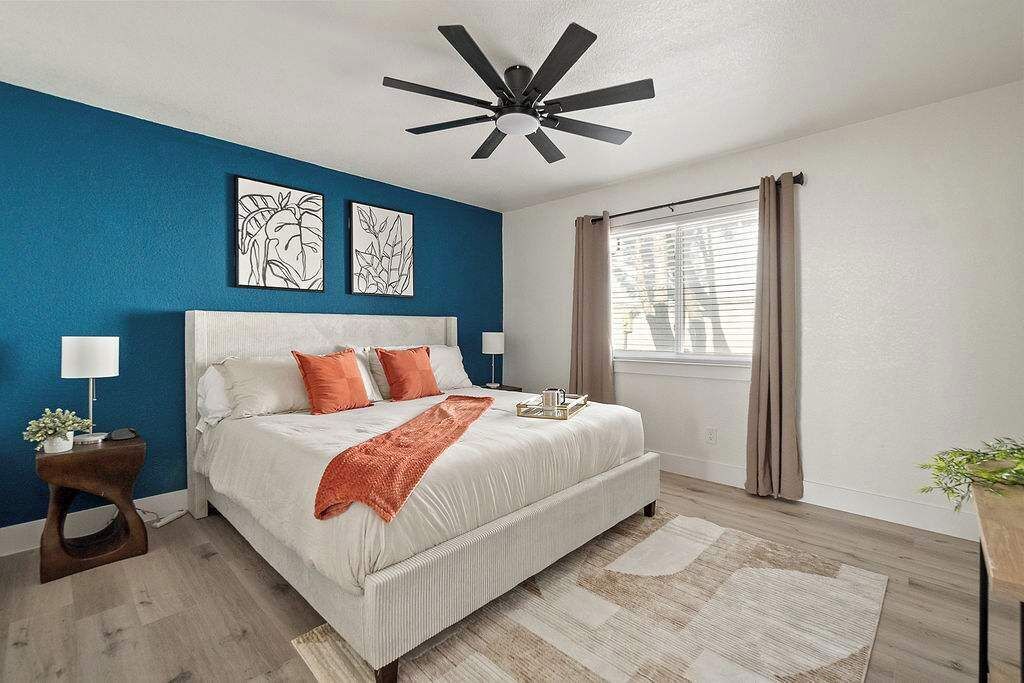 Un dormitorio con cama, ventilador de techo, ventana con cortinas y obras de arte en la pared.