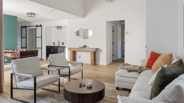 Ein modernes Wohnzimmer mit einer Couch, Sesseln, einem Couchtisch, einem Kamin und einer Küche im Hintergrund.