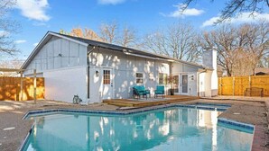 Ein Haus mit Schwimmbad, einer Holzterrasse und einem umzäunten Garten.