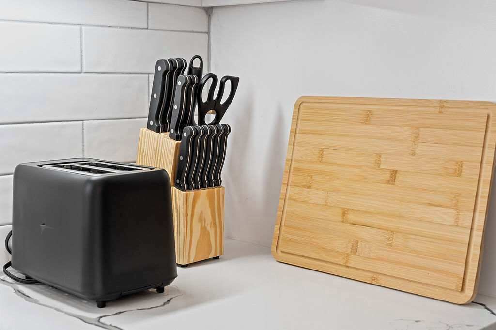 A kitchen with a toaster, a knife block, and a wooden cutting board.