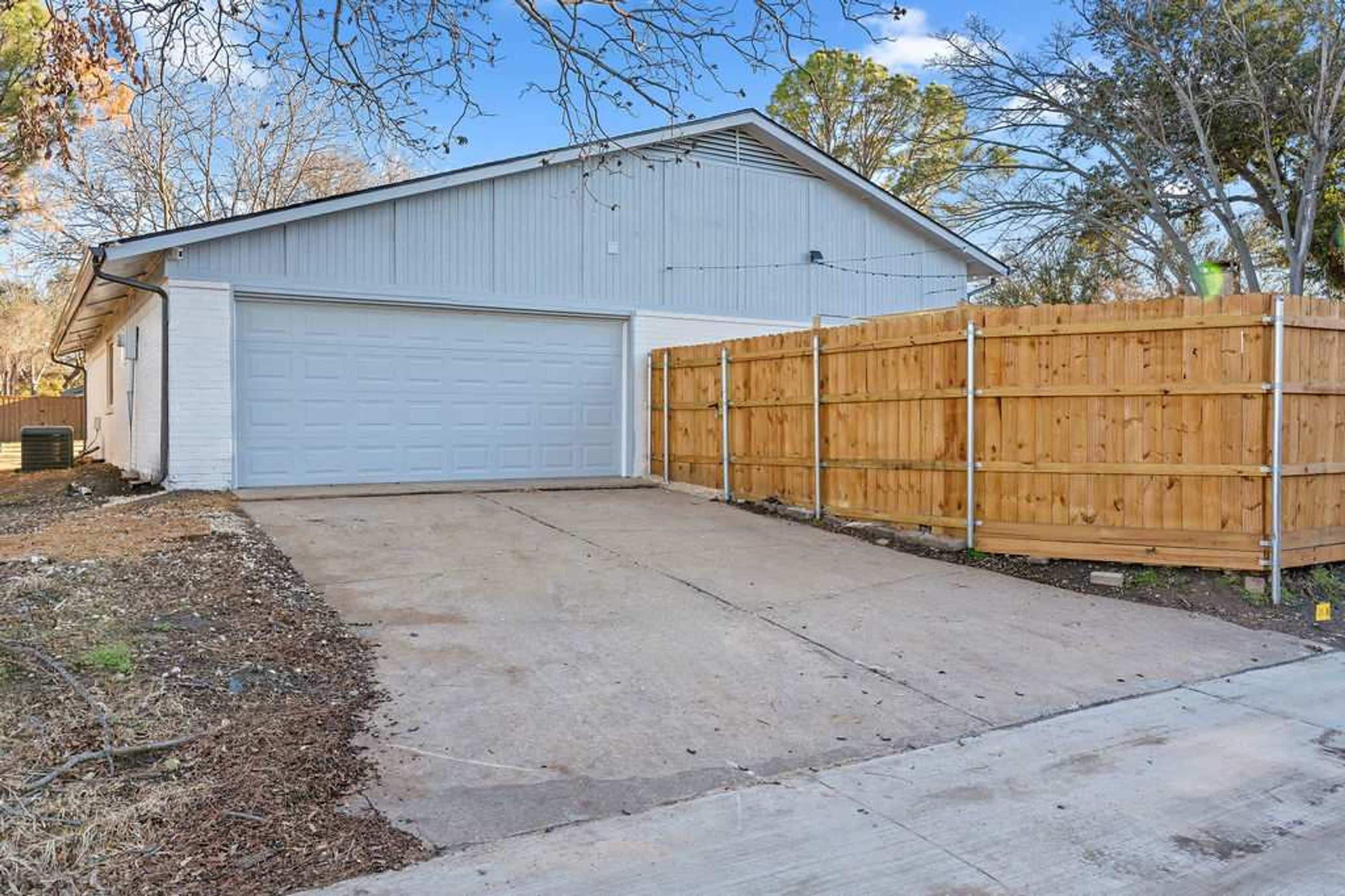 A single-story building with a garage door, a wooden fence, and a concrete driveway.