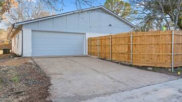 A single-story building with a garage door, a wooden fence, and a concrete driveway.