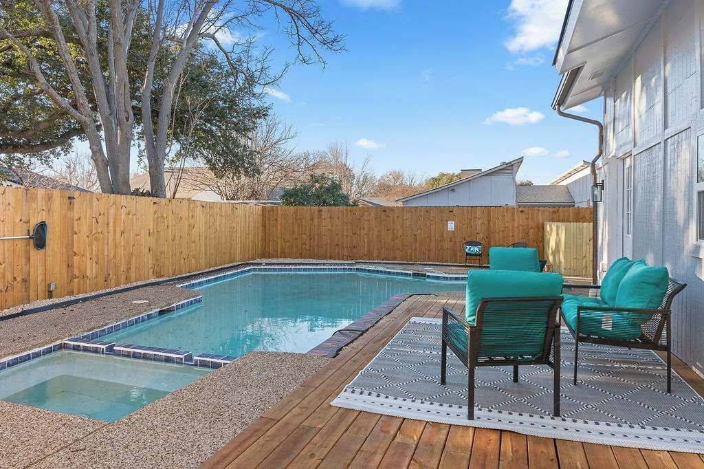 Un patio trasero con piscina, terraza de madera y mobiliario exterior.