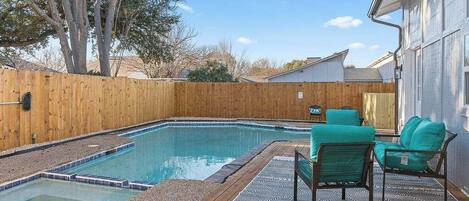 Un patio trasero con piscina, terraza de madera y mobiliario exterior.