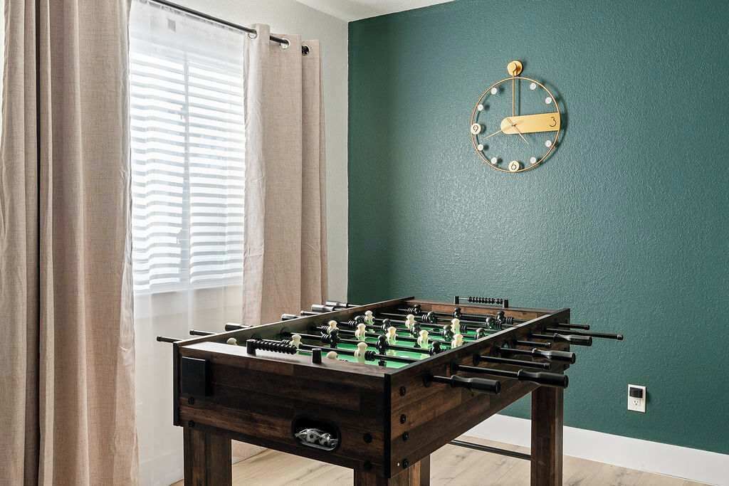 A room with a foosball table, a clock on the wall, and a window with curtains.
