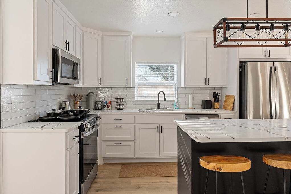 A kitchen with white cabinets, a stainless steel refrigerator, a microwave, and a stove.