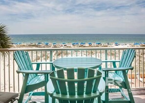 A balcony with turquoise Adirondack chairs and a table, overlooking a beach with umbrellas and people. - The Big Surf - Gulf View - Beach Pool and Dining (Gulf Shores)