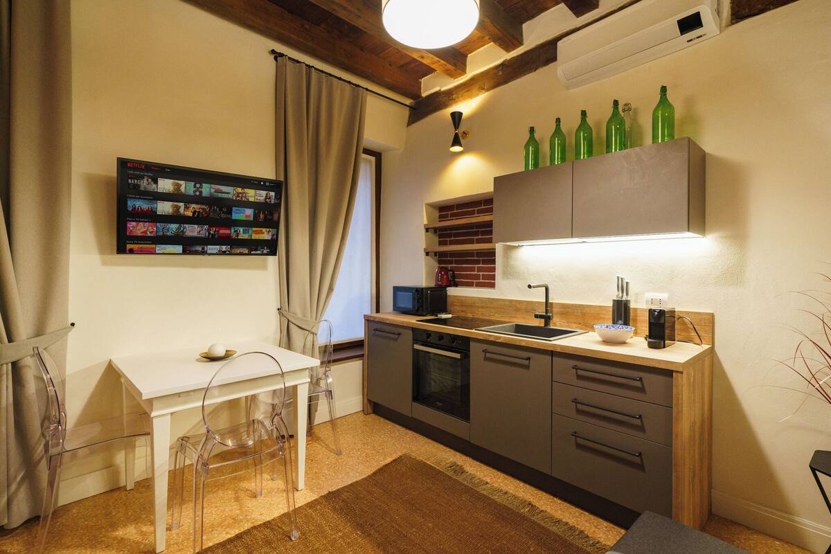 A compact kitchen with a white countertop, a microwave, and a sink. There are green bottles on the wall above the counter.