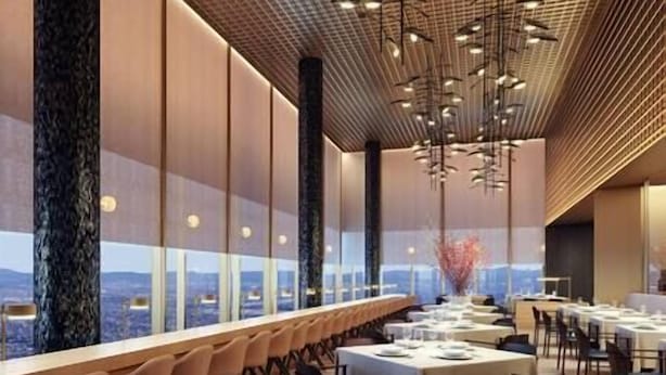 Un comedor moderno con una larga mesa dispuesta para una comida, grandes ventanales que ofrecen vistas y luminarias contemporáneas.