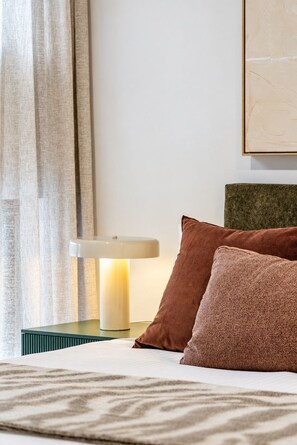 Ein ordentlich bezogenes Bett mit gemusterten Betttextilien, einer Nachttischlampe und einem Kopfkissen.