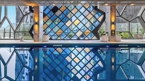 Un moderno vestíbulo de hotel con una pared de vidrio con patrón geométrico, una piscina y vistas a la ciudad.