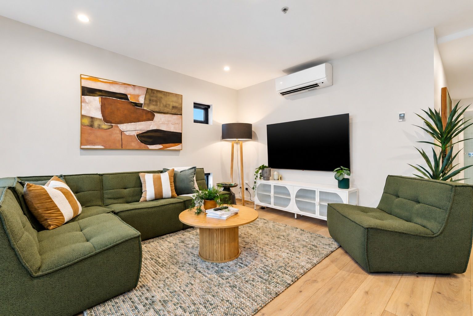A modern living room with a sectional sofa, a coffee table, a flat-screen TV, and a large plant.