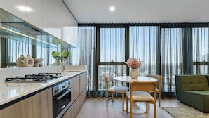 Una cocina moderna con una isla central, una zona de comedor con una mesa redonda y sillas, y un ventanal con cortinas traslúcidas.