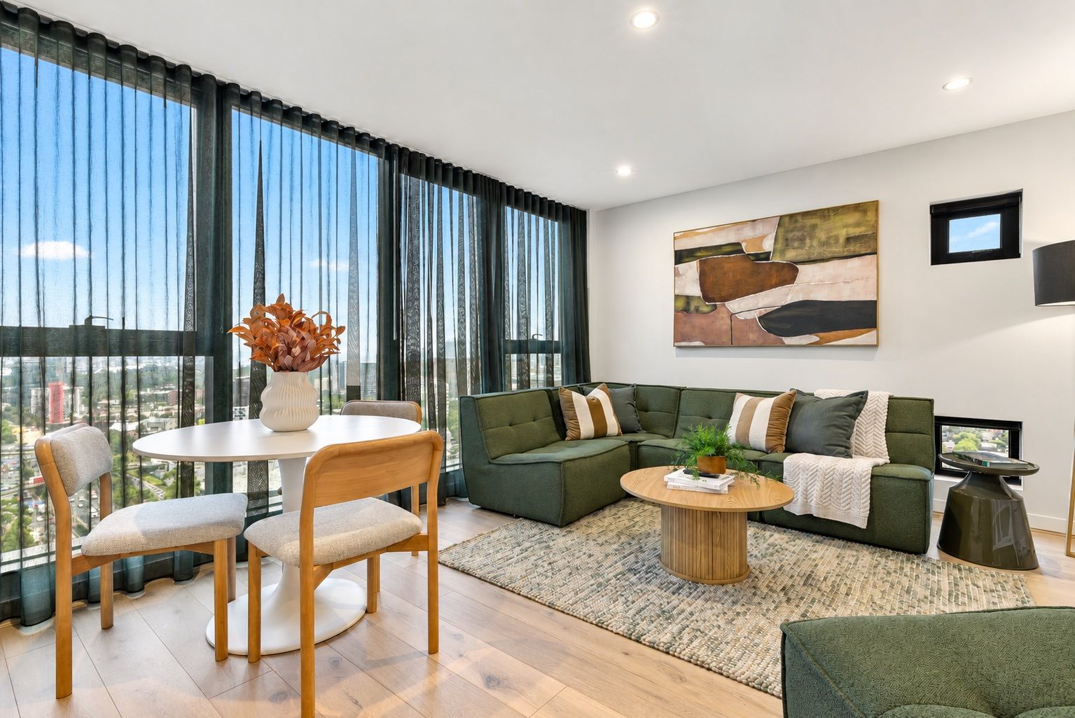 A modern living room with a green sofa, a round coffee table, and a dining area with chairs and a table.