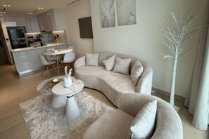 Ein modernes Wohnzimmer mit einer gebogenen Couch, einem runden Couchtisch und einem Essbereich mit weißem Tisch und Stühlen.
