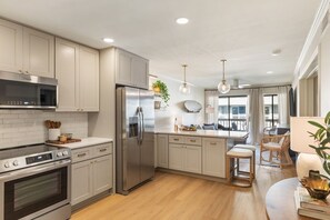 Una cocina moderna con electrodomésticos de acero inoxidable, piso de madera clara y un comedor con mobiliario de mimbre.