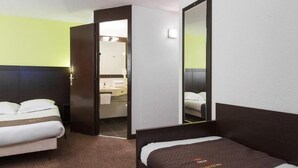 Une chambre d’hôtel avec deux lits, une salle de bain visible à travers une porte ouverte et un grand miroir sur un des murs.