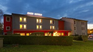 Un hôtel à la façade rouge et grise, doté de nombreuses fenêtres et d’une enseigne indiquant « ENZO HOTELS ».