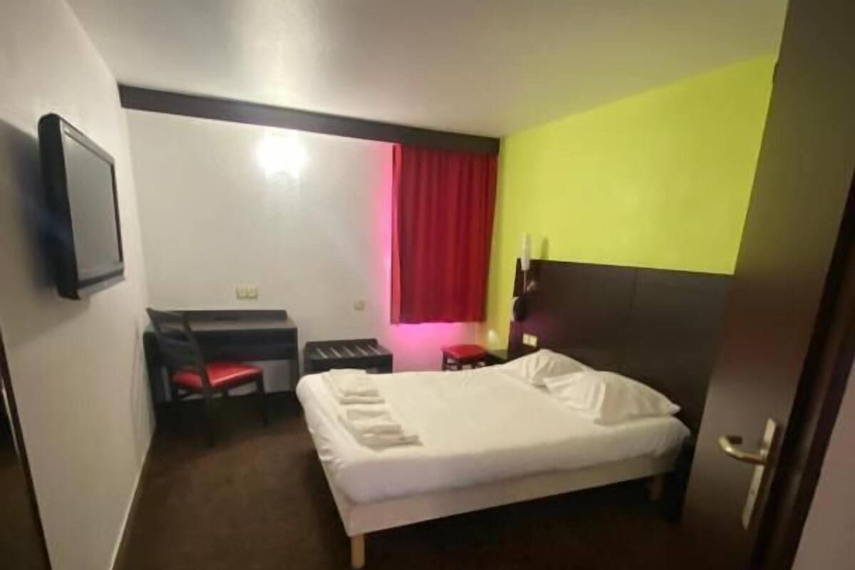 Une chambre d’hôtel avec un lit, un bureau, une chaise, une télévision et une porte.