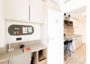 Et moderne køkken med hvide skabe, indbygget mikroovn og en lille bar med barstole.