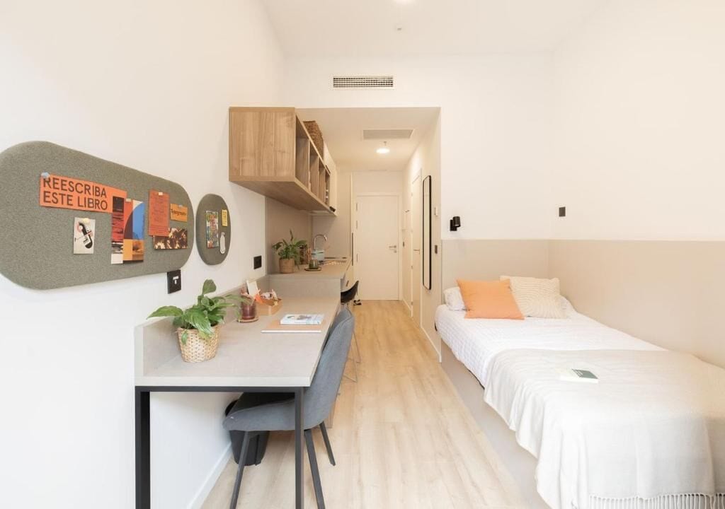 A compact hotel room with a kitchenette, a dining area, and a bed.