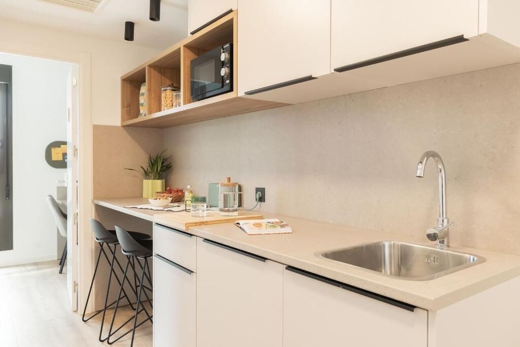 Une cuisine moderne dotée d’un évier en acier inoxydable, d’étagères en bois et d’un tabouret de bar.