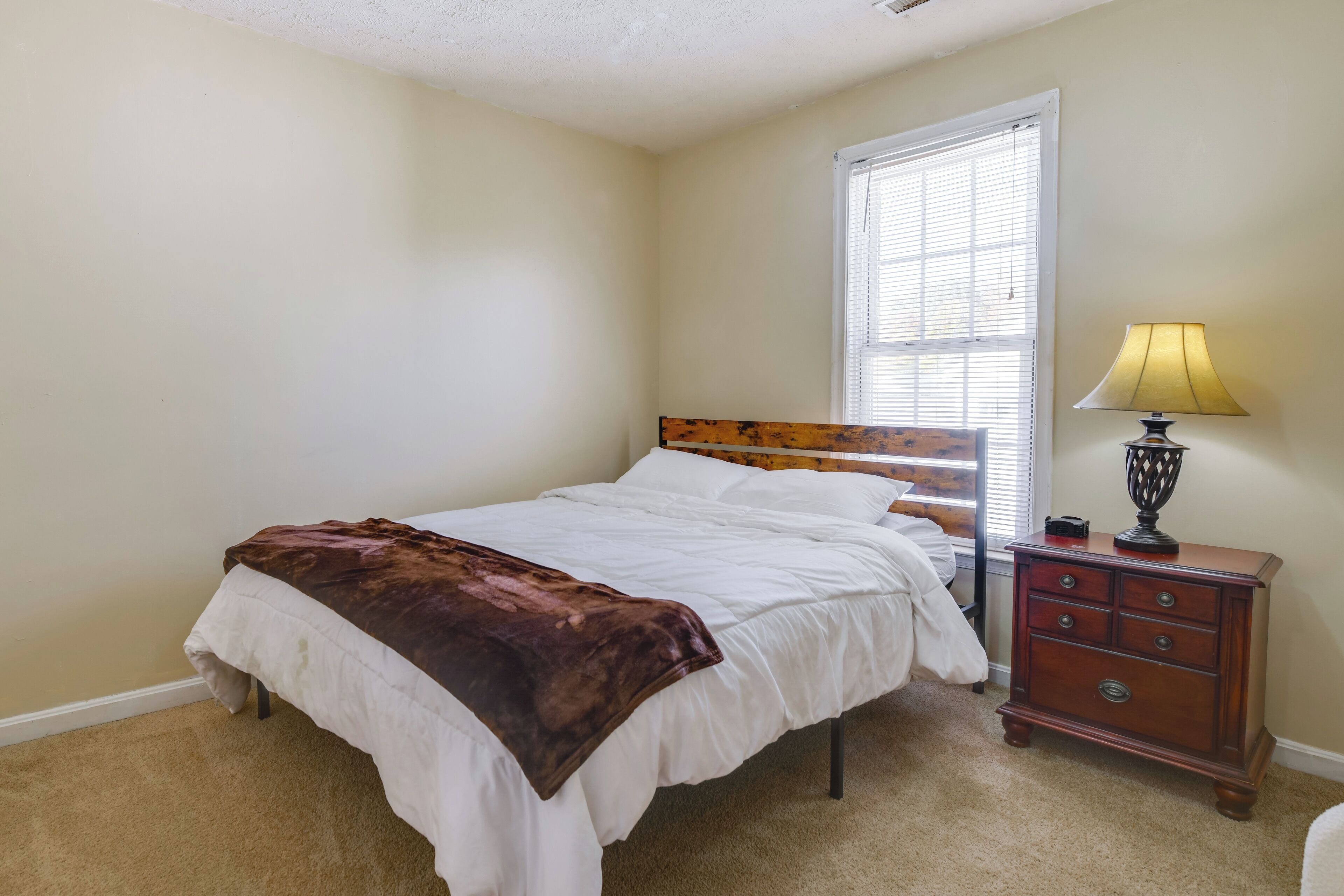 A bedroom with a bed, a nightstand, a lamp, and a window.