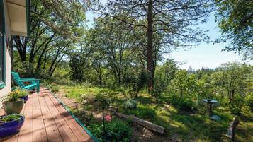 A wooden deck with outdoor seating, surrounded by lush greenery and trees.