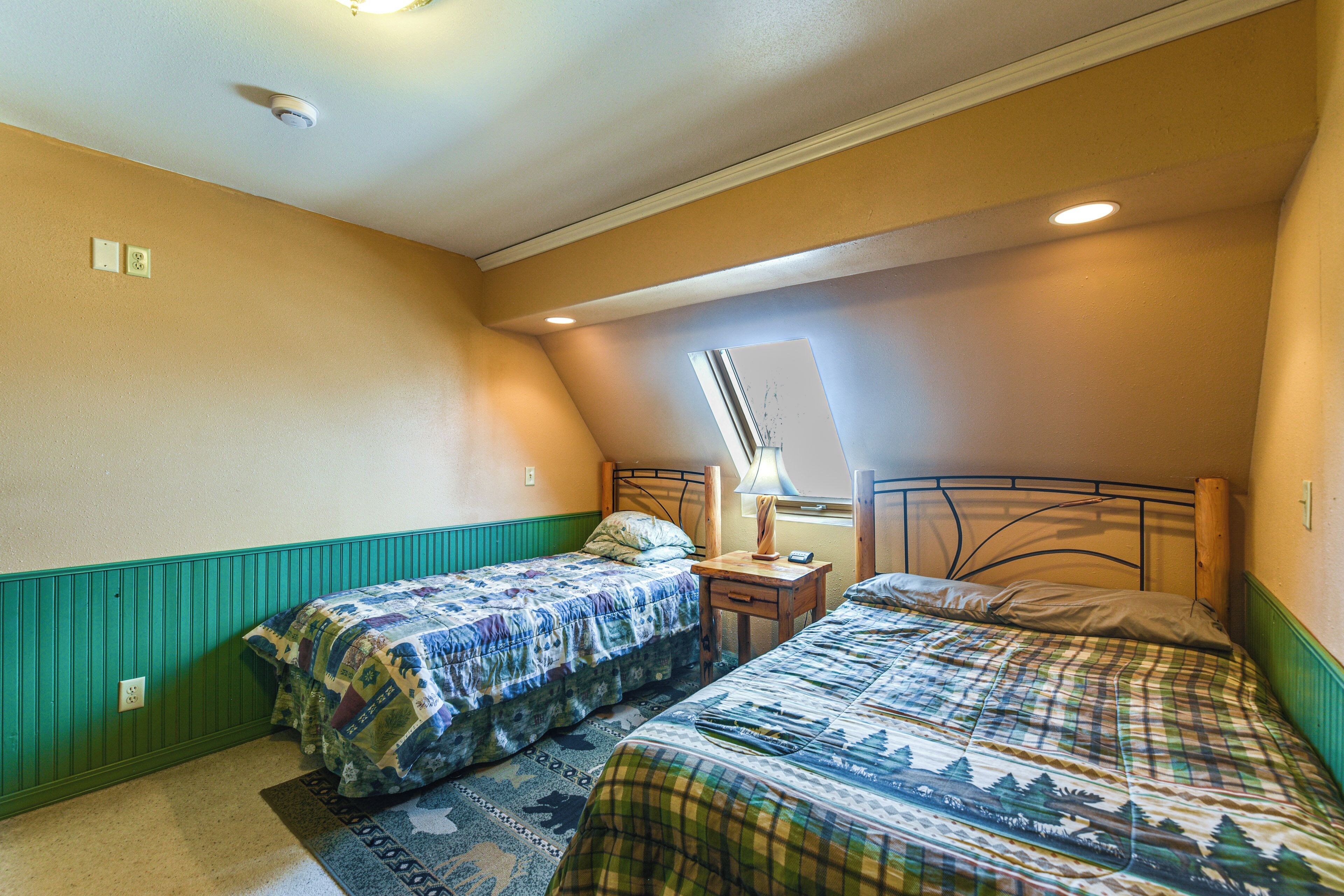 A bedroom with two beds, a window, and a nightstand with a lamp.